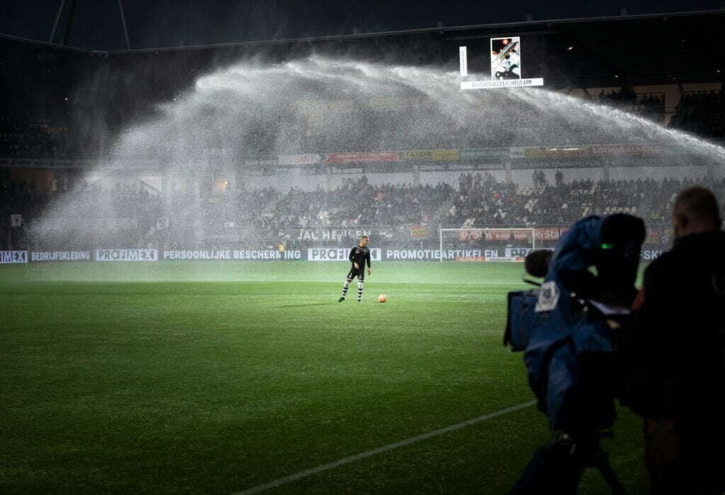 Image inside a football stadium. Football player is warming up while sprinklers are on.